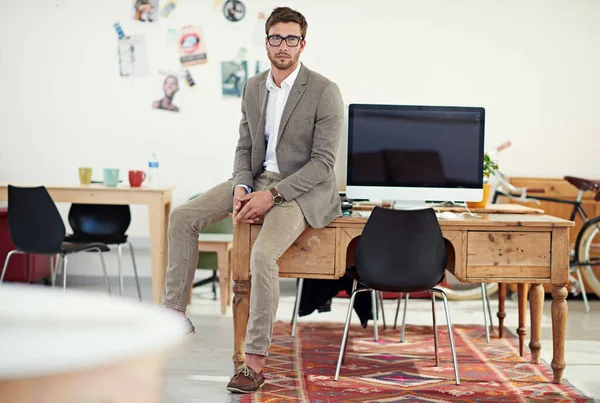 Lets get to work. Portrait of a casually-dressed young man sitting on his desk in an office