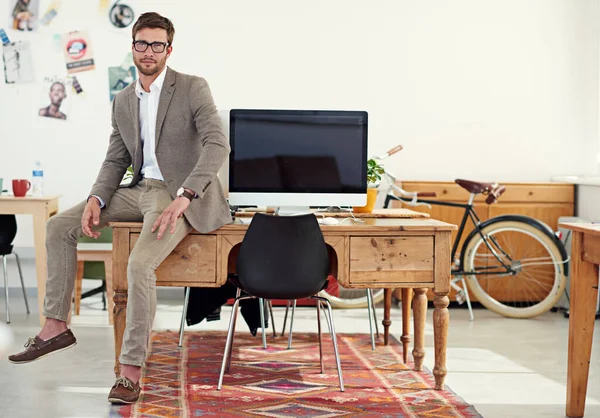 Its a great place to work. Portrait of a casually-dressed young man sitting on his desk in an office
