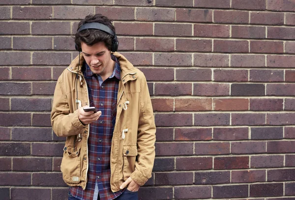 Take a sad song and make it better. a young man standing outdoors listening to music from his cellphone
