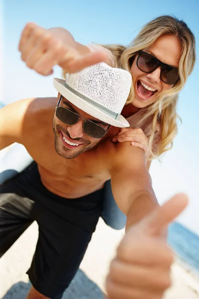 今までで最高の休暇 日当たりの良いビーチにいる遊び心のある若いカップルがカメラに親指を上げ — ストック写真