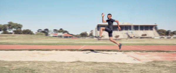 Long jump, athletics and fitness with a sports man jumping into a sand pit during a competition event. Health, exercise and training with a male athlete training for competitive track and field.