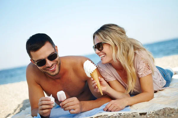 溶く前に食べなさい 晴れたビーチに横たわっている間にアイスクリームを食べる幸せな若いカップルは — ストック写真