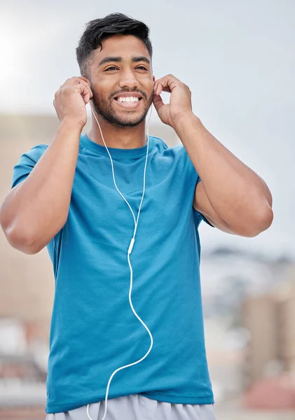Man, music and earphones for city exercise for wellness, training and running by blurred background. Happy runner, listening and streaming on internet, web or app to relax at workout in urban metro.