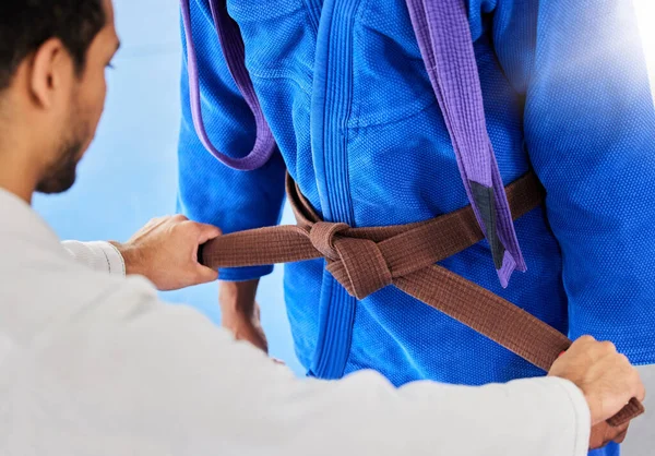 Coach, help and tie martial arts belt in dojo in graduation, progress or promotion to new class. Mentor, sensei and success with student in gym, helping from brown to purple level, karate or learning.