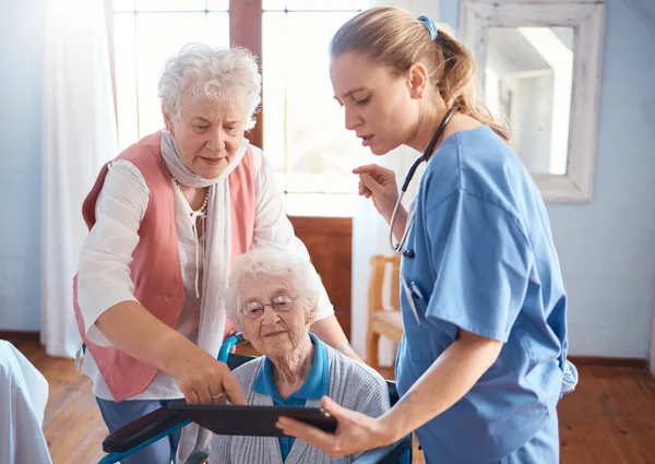 Doctor, tablet and visit for elderly care, consultation or healthcare diagnosis at old age home. Nurse or medical therapist working with touchscreen helping or consulting senior patient in wheelchair.