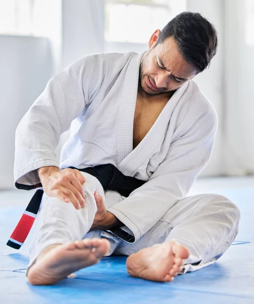 Injury, karate and man with knee pain after an accident in martial arts training in a wellness studio or dojo. Fitness, taekwondo and fighter with leg pain, emergency or joint pain after a workout.