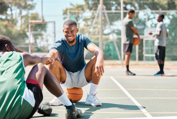 Sports, basketball and friends, men relax and fist bump on basketball court in happy summer. Friendship, teamwork and basketball player sitting on ground with friend and ball in community playground