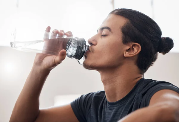 Tired, fitness or man drinking water in gym for fitness training or health workout exercise. Relax, sports or wellness athlete with water bottle for hydration, sport thirst or rest in studio.
