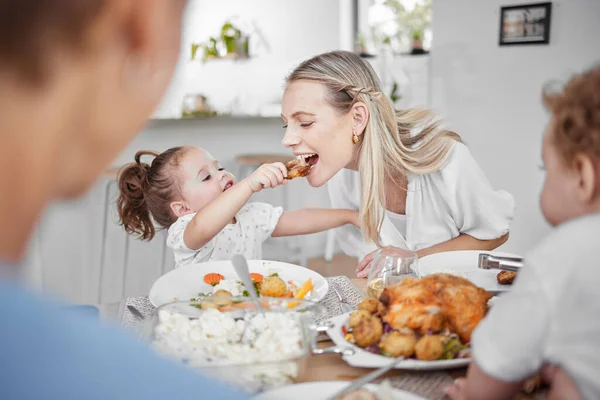 Happy family, mother and child eating chicken and vegetables in a healthy meal for dinner in Germany, Berlin. Food, nutrition and young girl feeding her hungry mom lunch at a home dining room table.