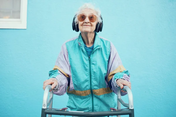 青い背景の壁に音楽 オーディオ ラジオを聞いてヘッドフォンを持つ都市 ファッションやシニア女性 町の歩行者と現代的で都会的で流行の服を着た自由 スタイル 高齢者の女性 — ストック写真