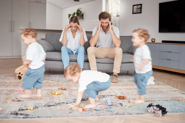Parents, stress and busy with an adhd child running around a home living room with energy or motion blur. Family children and headache with a hyperactive kid in a lounge with a stressed mom and dad.