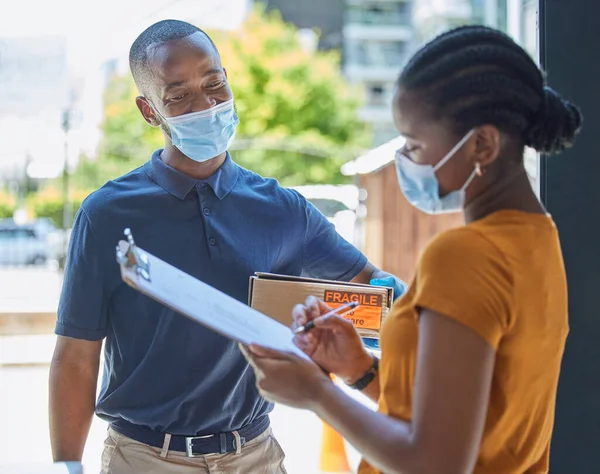 stock image Sign, covid and black woman with a delivery at the door with a happy delivery man in a face mask for safety compliance. Ecommerce, coronavirus and African girl customer with a clipboard for a box.