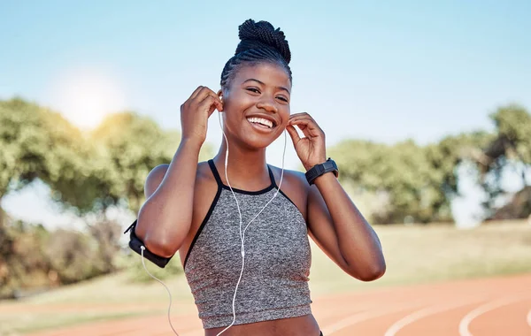 ランニング 幸せなワークアウトでフィットネスアプリのためのヘッドフォンや電話でトラック上の女性の肖像画 健康と健康のために実行中の笑顔ストリーミング音楽と技術 スポーツと黒の女性のランナー — ストック写真