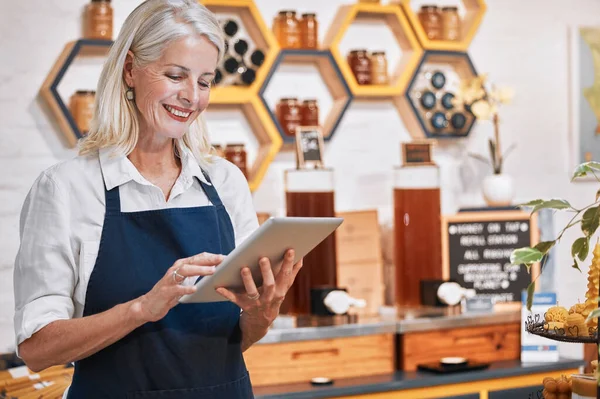 Happy small business owner, tablet or senior woman in honey retail store for research, communication or networking. Smile, honey or manager with social media app update, online store or order review.