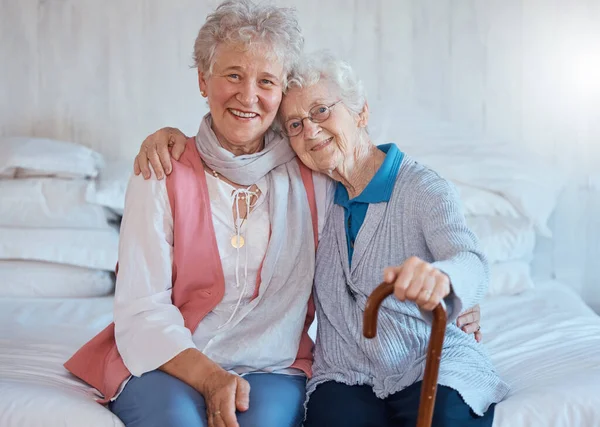 Senior friends, portrait and happy smile, hug and support on a bed in a retirement house, love and care. Elderly women, happiness and connection together in nursing home bedroom in life or friendship.