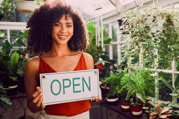 Plant shop, open sign and portrait of a woman with a small business standing in her retail nursery. Happy, smile and female entrepreneur from Brazil with a leaf, nature or organic store holding board.