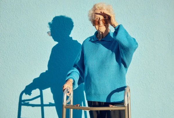 移動歩行者の屋外を保持しながら 青い壁の背景に高齢者の女性と肖像画 影と障害 一人で外に立つ成熟した女性の健康 ハンディキャップ ファッション — ストック写真