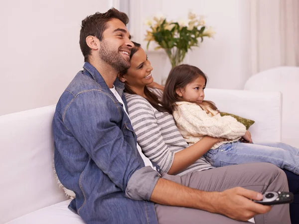 Lets watch some cartoons. a young family sitting together on a sofa watching television