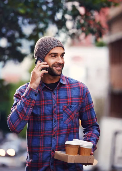 stock image Im bringing coffee. a handsome young man in winter wear talking on his mobile phone while holding cups of coffee