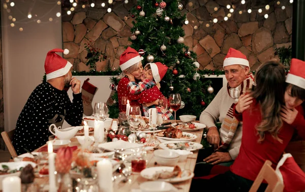 Family, generations and Christmas dinner party with men, women and children smile, eat and drink together in dining room. Happy family, kids, couple and grandparents celebrate holiday hug at table