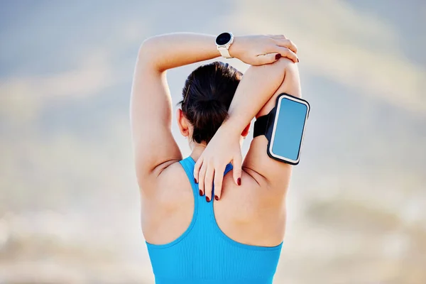 stock image Woman, stretching arms and back view in outdoor for fitness track on smartphone and healthcare exercise. Cardio training workout, sports motivation and athlete stretch body for runner performance.