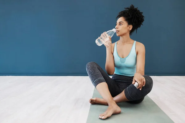 Tired, fitness or woman drinking water in gym for fitness training, workout exercise or health. Athlete, yoga or relax girl with water bottle for sport hydration, mockup or rest energy in studio.
