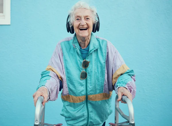 クールなジャケットやヘッドフォンで無料で音楽 ラジオやオーディオをストリーミング肖像画 ヒップホップや古い女性 ファッション 幸せな先輩が青い壁の背景を持つ歌を聞いて — ストック写真