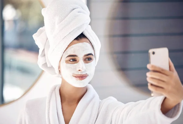 Woman, facial mask and phone selfie after morning shower, wellness and healthy skincare, makeup product and cleaning in bathroom at home. Beauty, face mask cosmetics and female taking photo on mobile.