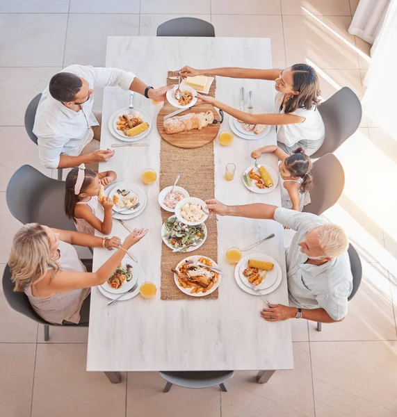 Family, food and lunch with love and care at the dining room table to eat and drink. Group, grandparents and parents with kids eating a delicious meal in a family home with a happy family in top view.