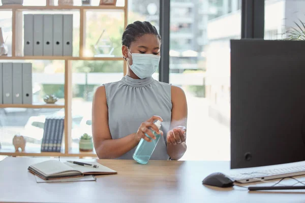 Covid, mask and hand sanitizer with a business black woman cleaning while working in her office. Health, safety and sanitizing with a female employee using disinfectant during the corona virus.