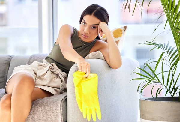Tired, portrait and cleaning of a woman with gloves feeling fatigue in a house living room sofa. Portrait of a young person spring cleaning a home lounge feeling bored and frustrated on a couch.