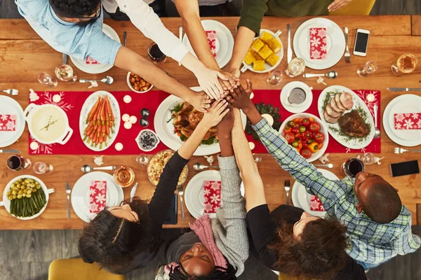 Christmas, high five and food with a group of friends sitting around a dinner table together for celebration. Thanksgiving, hands and meal with a team enjoying a lunch on a wooden surface from above.