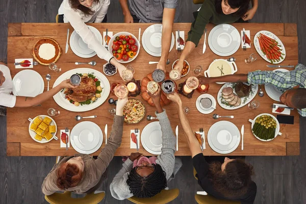 Food, top view and friends toast at a table in celebration of thanksgiving at a party or social event together. Cheers, support and happy people with diversity, support and trust enjoy a dinner meal.