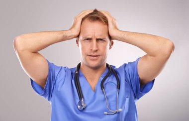 Ameliyat çok stresli olabilir. Kafası karışmış bir doktorun elleri başının üstünde durduğu bir stüdyo resmi.