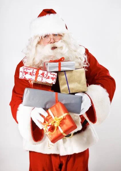 シニアマン サンタクラスや配達 お祝いや休日のイベントのためのスタジオで白い背景によって提示します 退職高齢者 お祝いのクリスマスの衣装やモックアップを背景にクリスマスの小包ギフトボックス — ストック写真