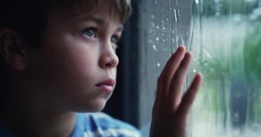 Çocuklar, sıkılmış ve yağmur yağıyor. Pencerenin kenarında duran üzgün bir çocuk, ıslak kış havasını düşünüyor ya da bakıyor. Çocuklar, cam ve depresyon. Bir erkek çocuk evinde yalnız başına üzüntü hissediyor..