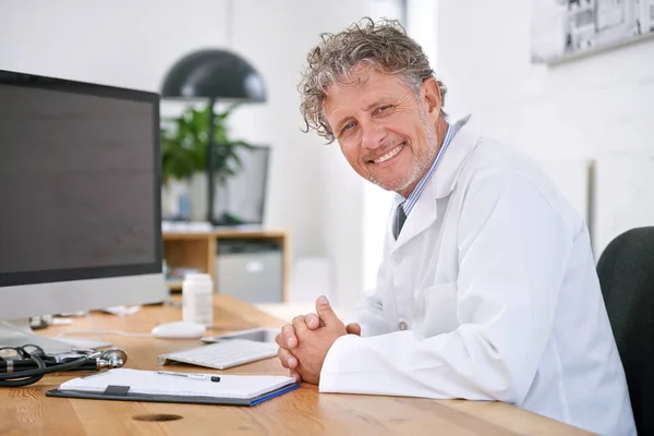 我对每个病人都给予个别的治疗 一个面带微笑的成熟医生坐在办公室桌子旁的画像 — 图库照片