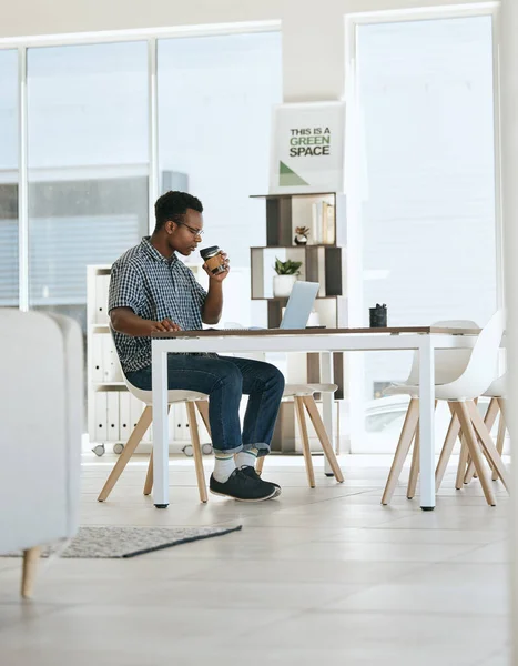 Black man, coffee drinking and office with laptop, table and thinking in marketing startup business. Man, drink espresso or tea at desk with computer, reading and planning for digital marketing job.