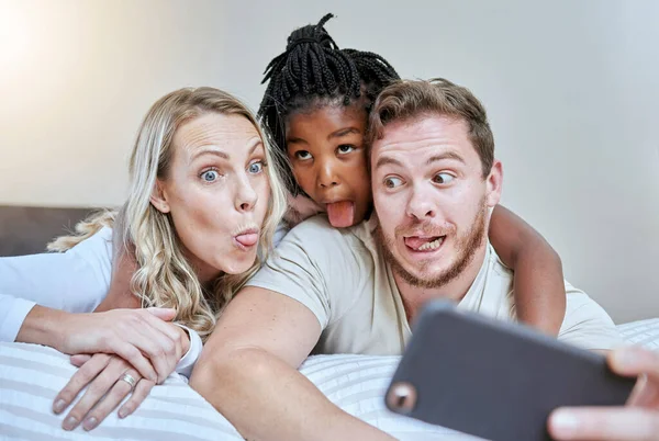 Stock image Child, parents or comic face for phone selfie in house, hotel or home bedroom on social media, memory vlog or fun. Mother, father or black girl on mobile photography technology with tongue expression.