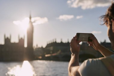Big Ben 'in Londra' da telefonla fotoğraflarını çeken adam, seyahat ve turizm, tatil gezileri, tarihi yerler, binalar ve tatiller. İngiltere 'de turist, gezici resimler ve saat kulesi.