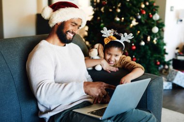 Noel 'de, siyah baba ve kızı dizüstü bilgisayarlarıyla internette sosyal medya okuyup gülümsüyor. Tatil, aile evinde, oturma odasında ve internet uygulamasında mutlu ve bağlanan bir baba ve kız..