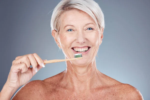 Dental, studio and senior woman brushing teeth on a gray background. Oral health, wellness and routine of elderly female from Canada holding toothbrush and cleaning teeth for hygiene and oral care.