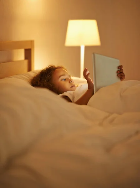Picking tonights dream. A cute little girl lying in a double bed and playing on a tablet