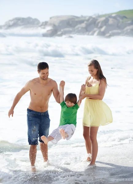 ウィー ビーチを歩いている間に彼らの息子を揺らしている2人の両親 — ストック写真