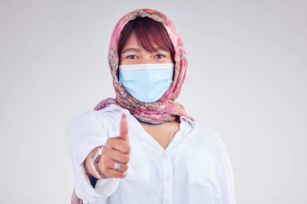 Covid face mask, muslim woman and thumbs up, portrait and vaccine yes vote, safety compliance and emoji, health risk and policy on studio background. Corona virus, thumb up and islamic female hijab.