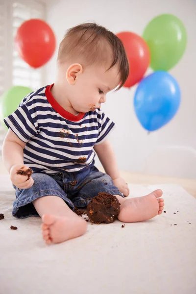他在给他的生日蛋糕取样 一个坐在家里的小男孩 背对着气球 — 图库照片