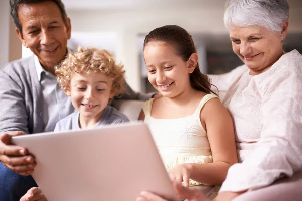 有祖父母的孩子两个孩子和他们的祖父母坐在沙发上使用数码平板电脑的照片 — 图库照片