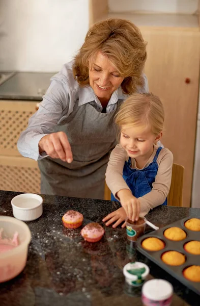Having fun in the kitchen with granny. A little girl decorating cupcakes with the help of her grandmother