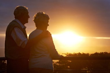 Their golden anniversary. an elderly couple looking at the view at sunset clipart