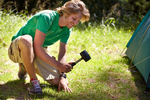 stock image Setting up camp. A handsome young man securing a tent at the campsite